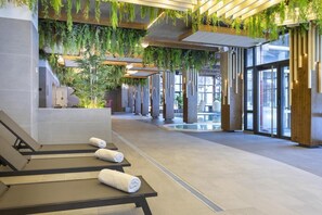 Uma área de spa moderna com cadeiras reclináveis, piscina e plantas penduradas.