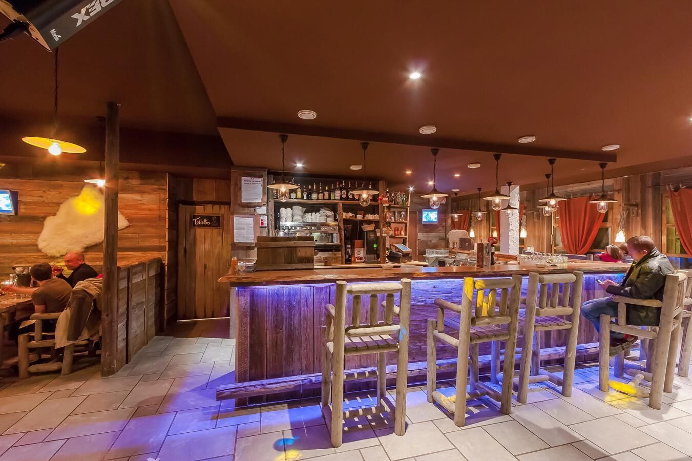 Un espace bar avec des meubles en bois, un comptoir et un éclairage suspendu.