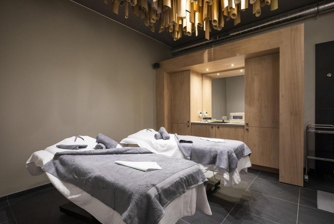 A modern spa room with two treatment beds, wooden cabinets, and a visible bathroom area.