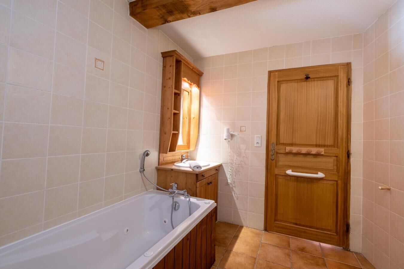 A bathroom with a bathtub, wooden vanity, and a wooden door.