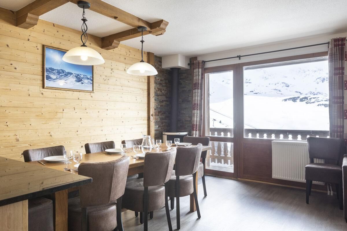 En matplats med träpanel på väggarna, ett stort fönster med utsikt över snöklädda berg och en öppen spis.