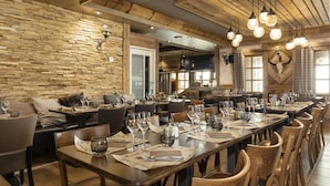 A restaurant with a long wooden table set for dining, a stone wall, and a rustic ceiling. - Wifi, 100m from ski slopes, fitness, swimming pool, sauna, jacuzzi, hammam, balcony (Val Thorens)