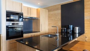 A modern kitchen with wooden cabinets, a black countertop, stainless steel appliances, and a black backsplash. - Wifi, 100m from ski slopes, fitness, swimming pool, sauna, jacuzzi, hammam, balcony (Val Thorens)