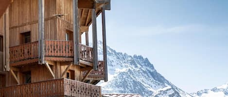 A wooden chalet with multiple balconies, set against a backdrop of snow-covered mountains.