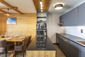 Moderni keittiö, jossa on keskeinen saareke, integroidut kodinkoneet ja puinen ruokailutila.