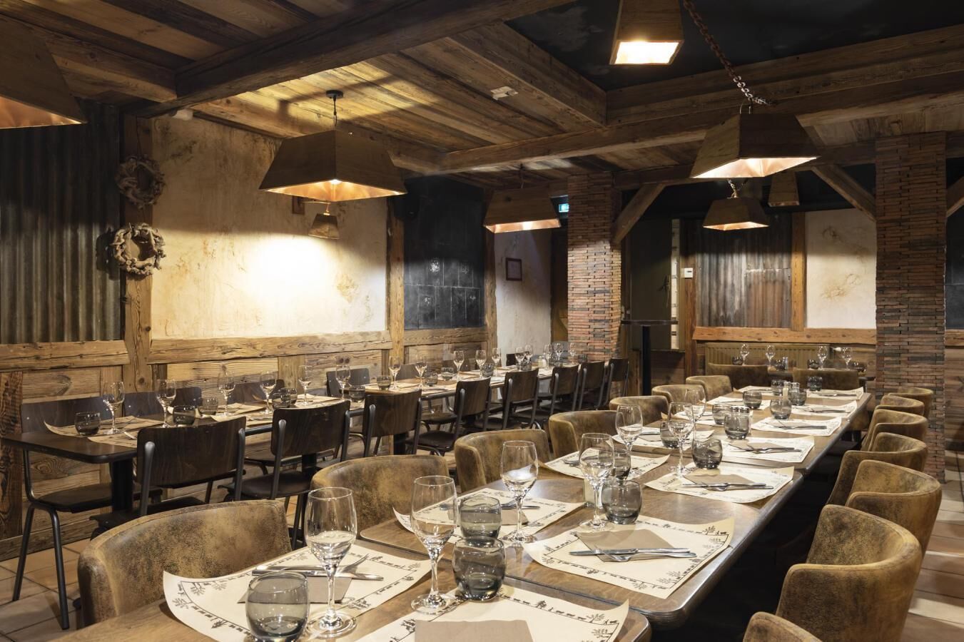 Een lange eettafel met stoelen, houten balken in het plafond en rustieke decoratie.