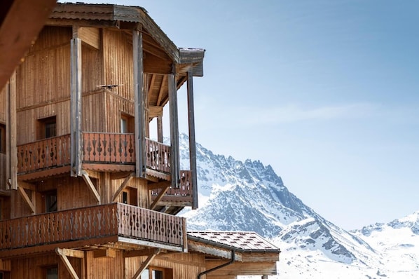 A wooden chalet with multiple balconies, set against a backdrop of snow-covered mountains.