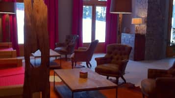 A spacious living room with a stone wall, leather armchairs, a wooden coffee table, and a large window with curtains.