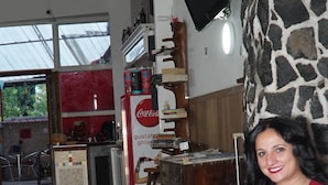 A person sitting on a red couch in a room with a tiled floor, a stone wall, and a Coca-Cola refrigerator. - B&B Cappotto Civico 48 (Pompei)