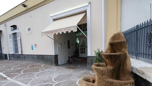 A building entrance with a stone fountain, a patterned pavement, and a metal fence. - B&B Cappotto Civico 48 (Pompei)
