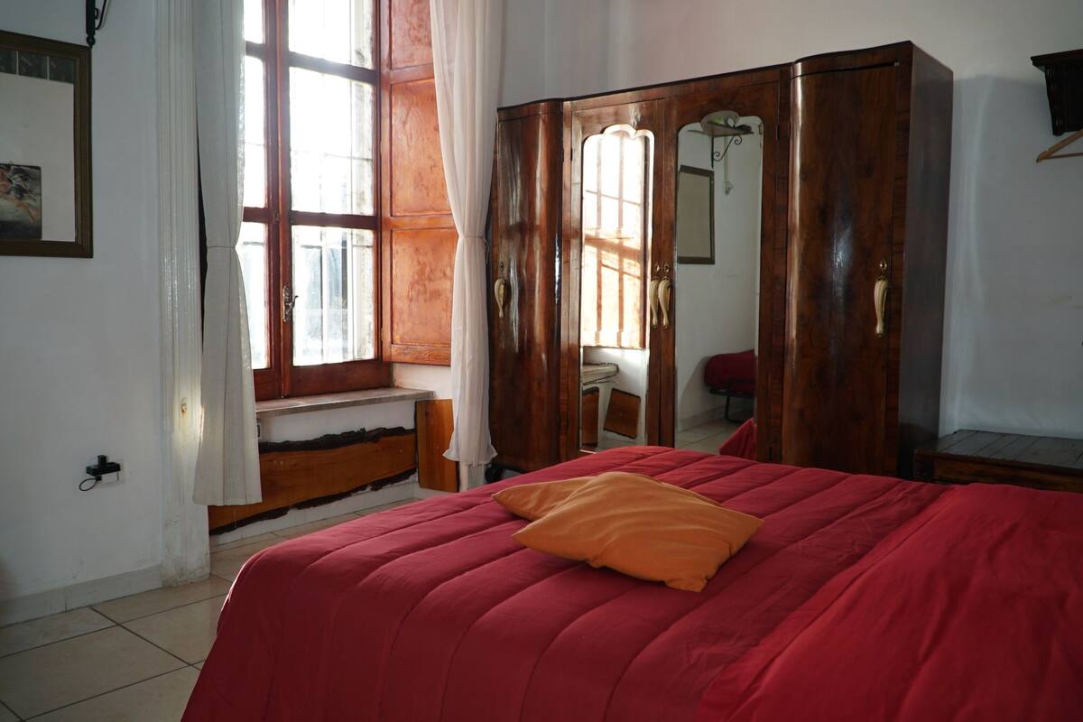 A room with a bed, a wardrobe, a window with curtains, and a mirror.