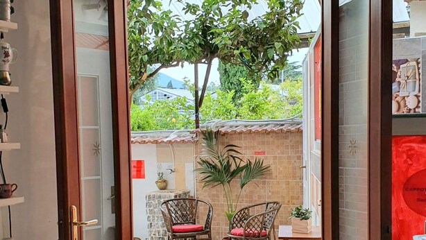 A room with a wooden door leading to an outdoor area with two wicker chairs and a small table. - B&B Cappotto Civico 48 (Pompei)