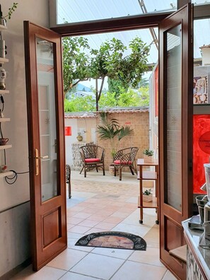 A room with a wooden door leading to an outdoor area with two wicker chairs and a small table. - B&B Cappotto Civico 48 (Pompei)