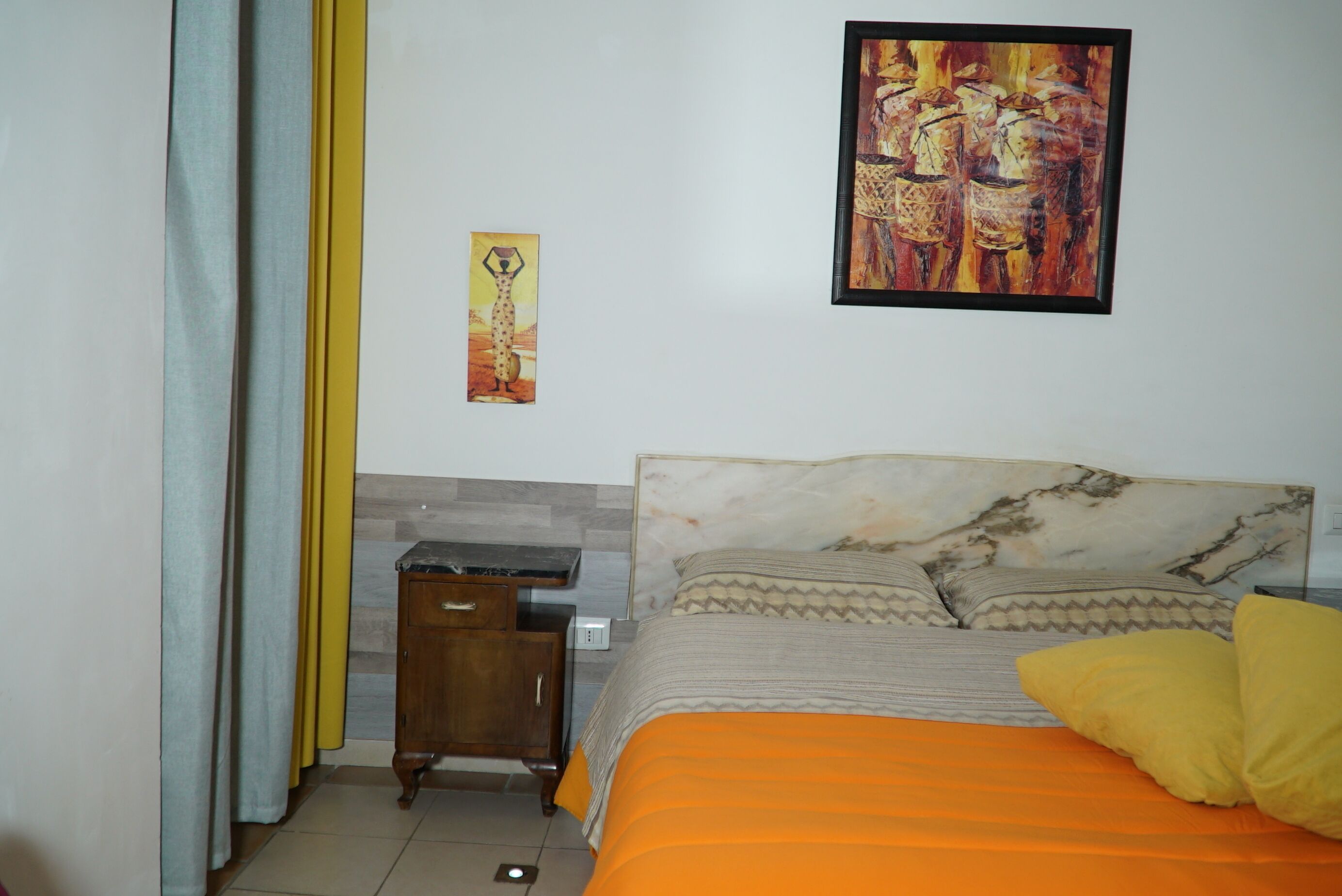A bedroom with a bed, a nightstand, a wall-mounted painting, and a window with curtains.