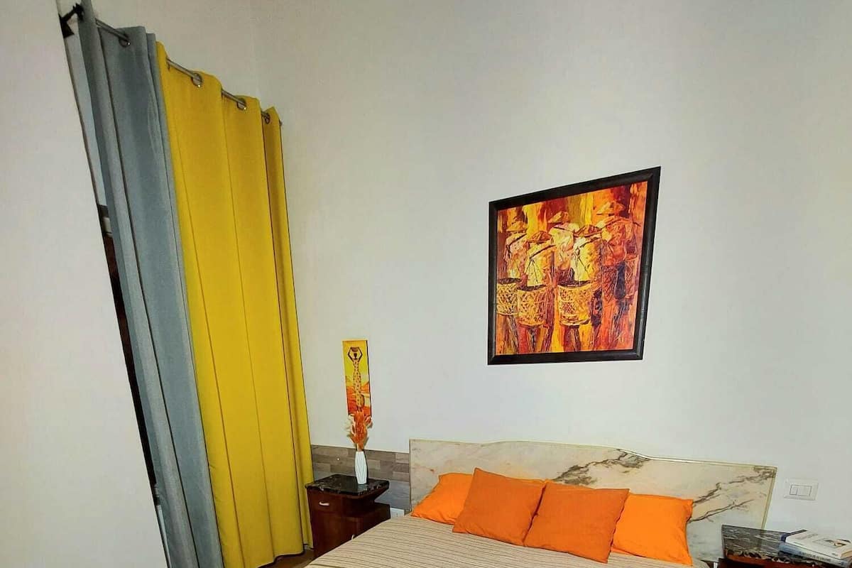 A bedroom with a large bed, a nightstand, a painting on the wall, and curtains.