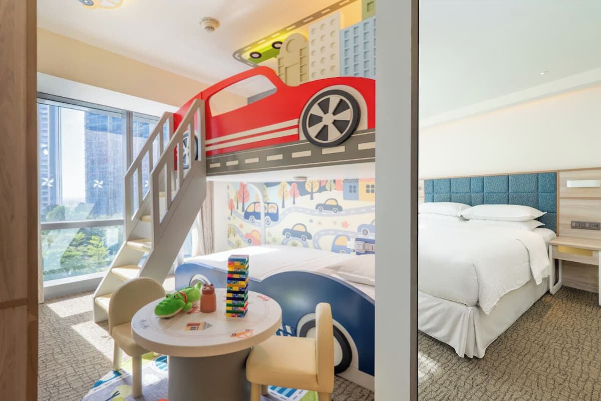 Ein Kinderzimmer mit Etagenbett, Spieltisch und Spielzeug sowie Blick auf eine Stadtlandschaft.