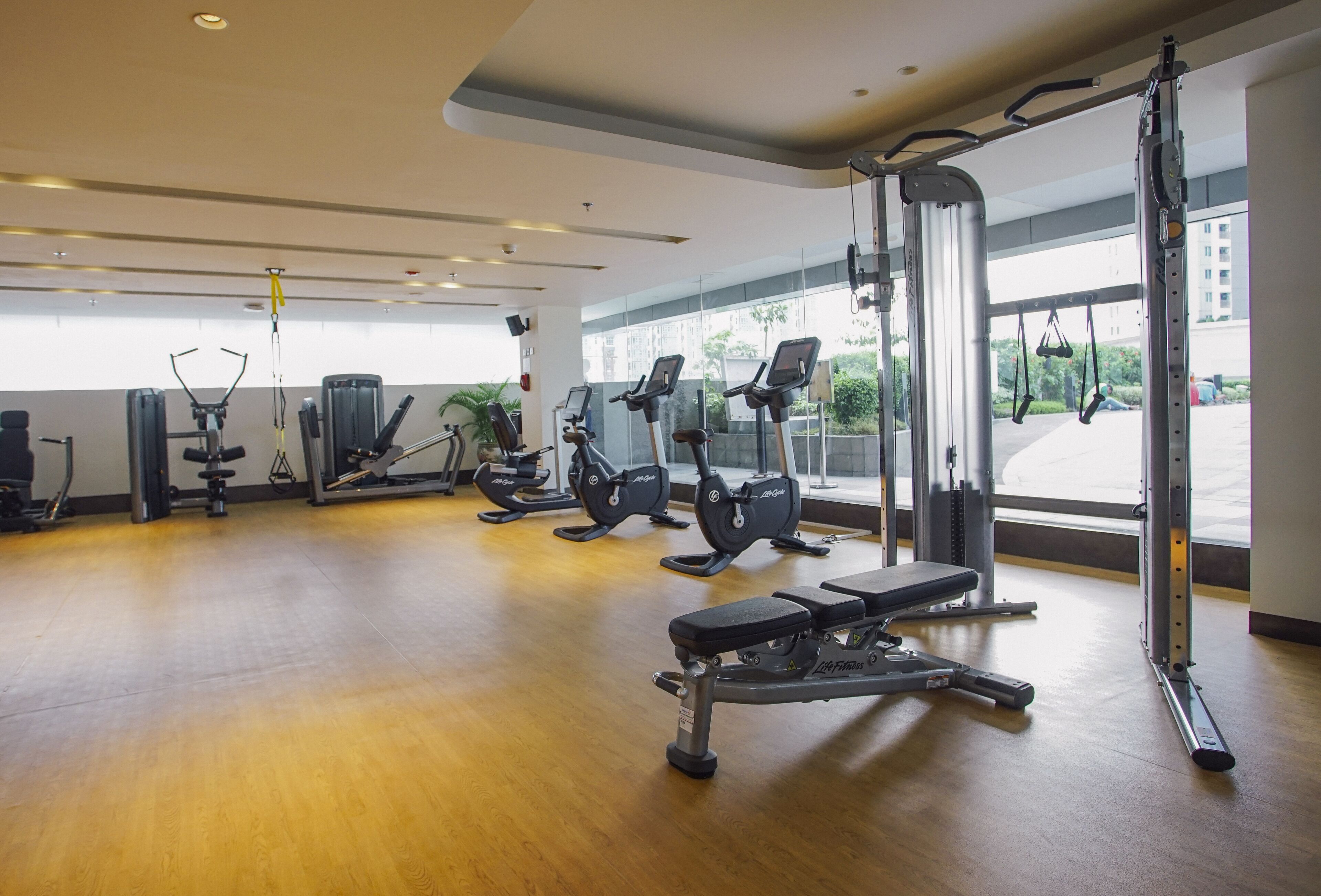 Uma academia com diversos equipamentos de exercícios, grandes janelas e piso de madeira.