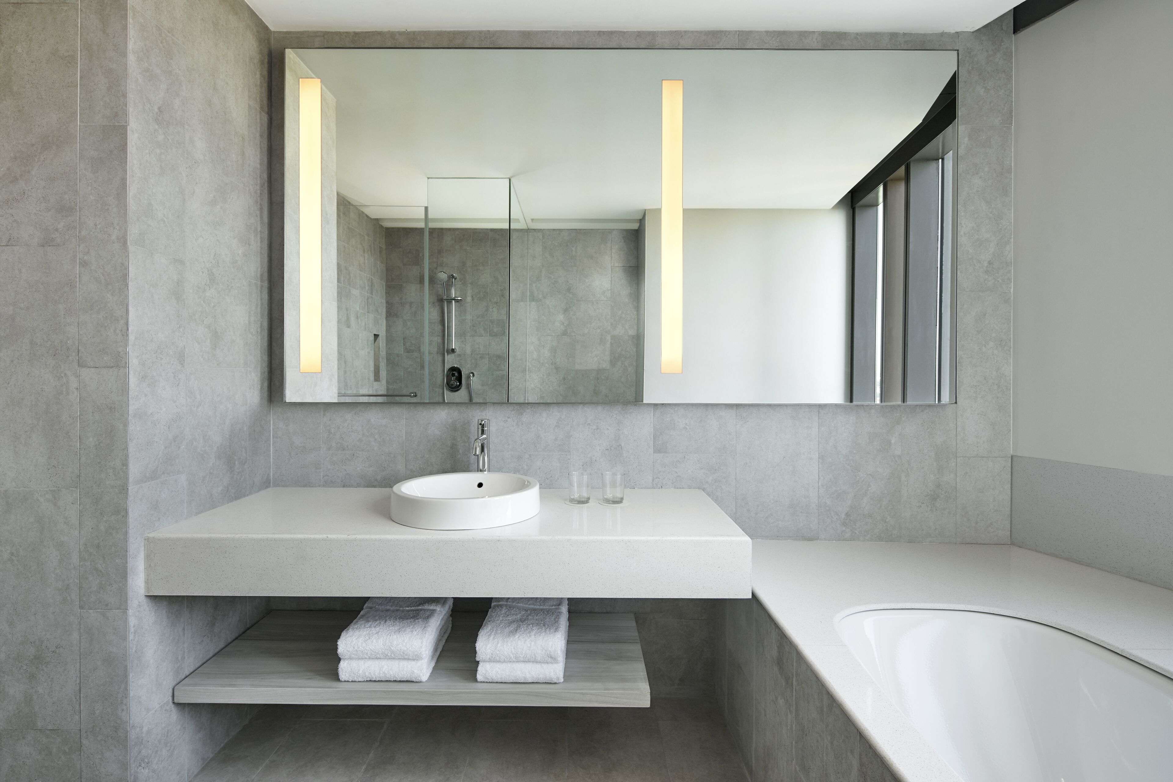 A modern bathroom with a large mirror, a white sink, and a bathtub.