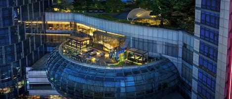 A modern hotel with a curved glass facade, rooftop garden, and multiple dining areas.