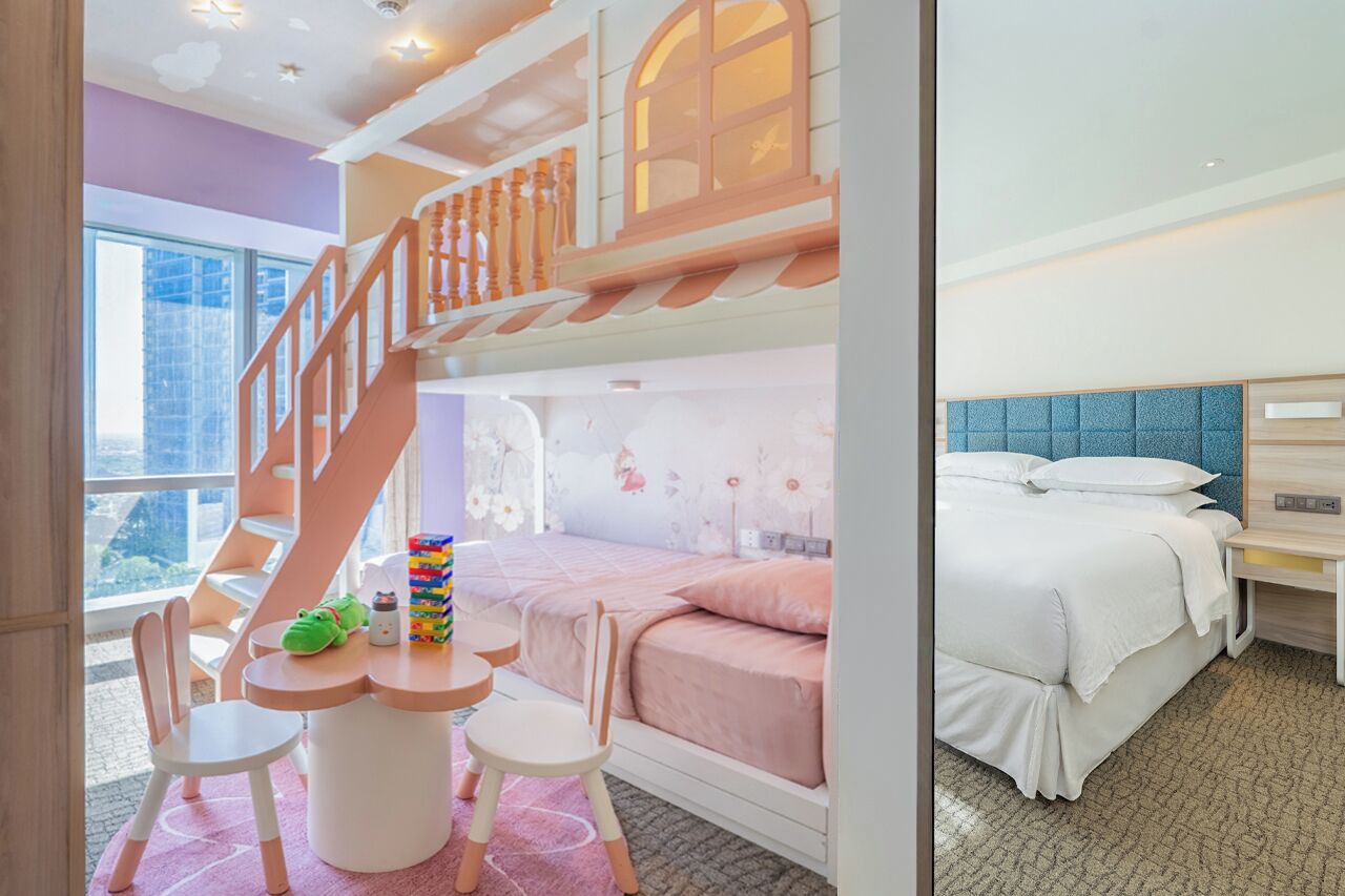 A children's play area with a wooden staircase, a pink play table, and a bed with a blue headboard.