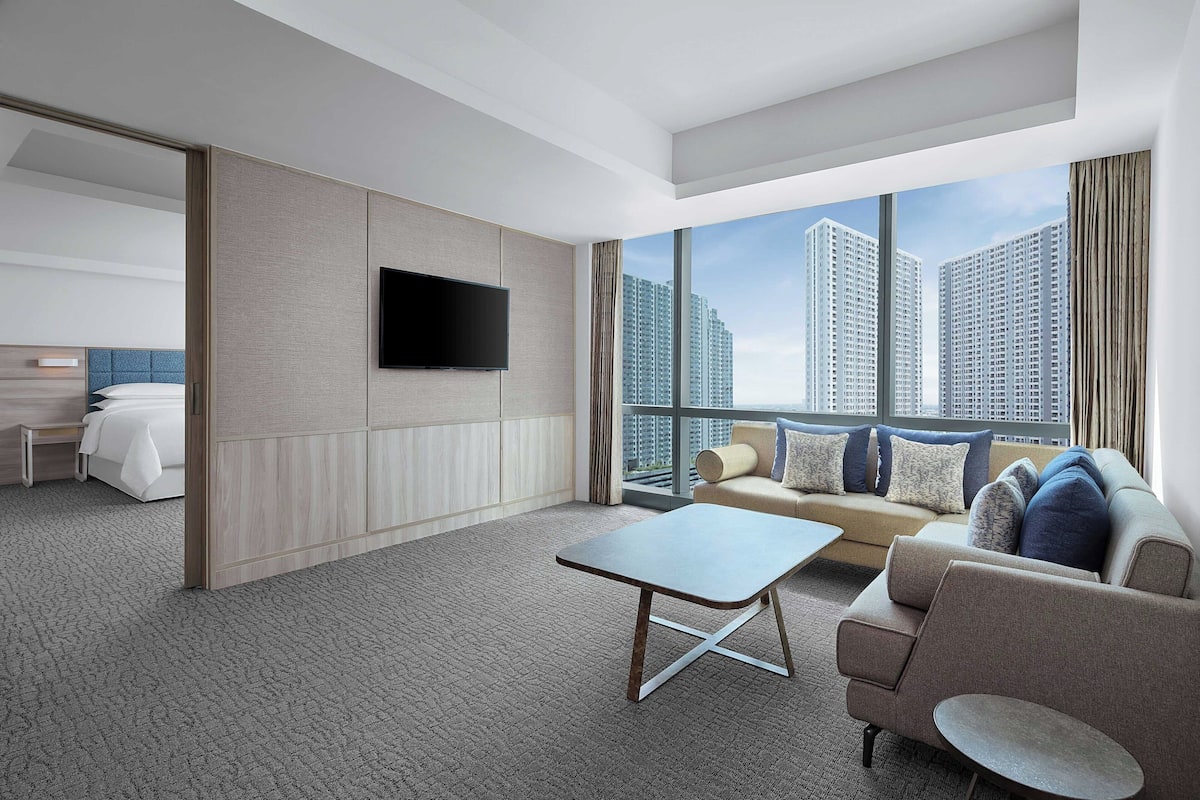 Ein modernes Hotelzimmer mit großem Fenster, Flachbildfernseher, Sofa, Couchtisch und Bett.