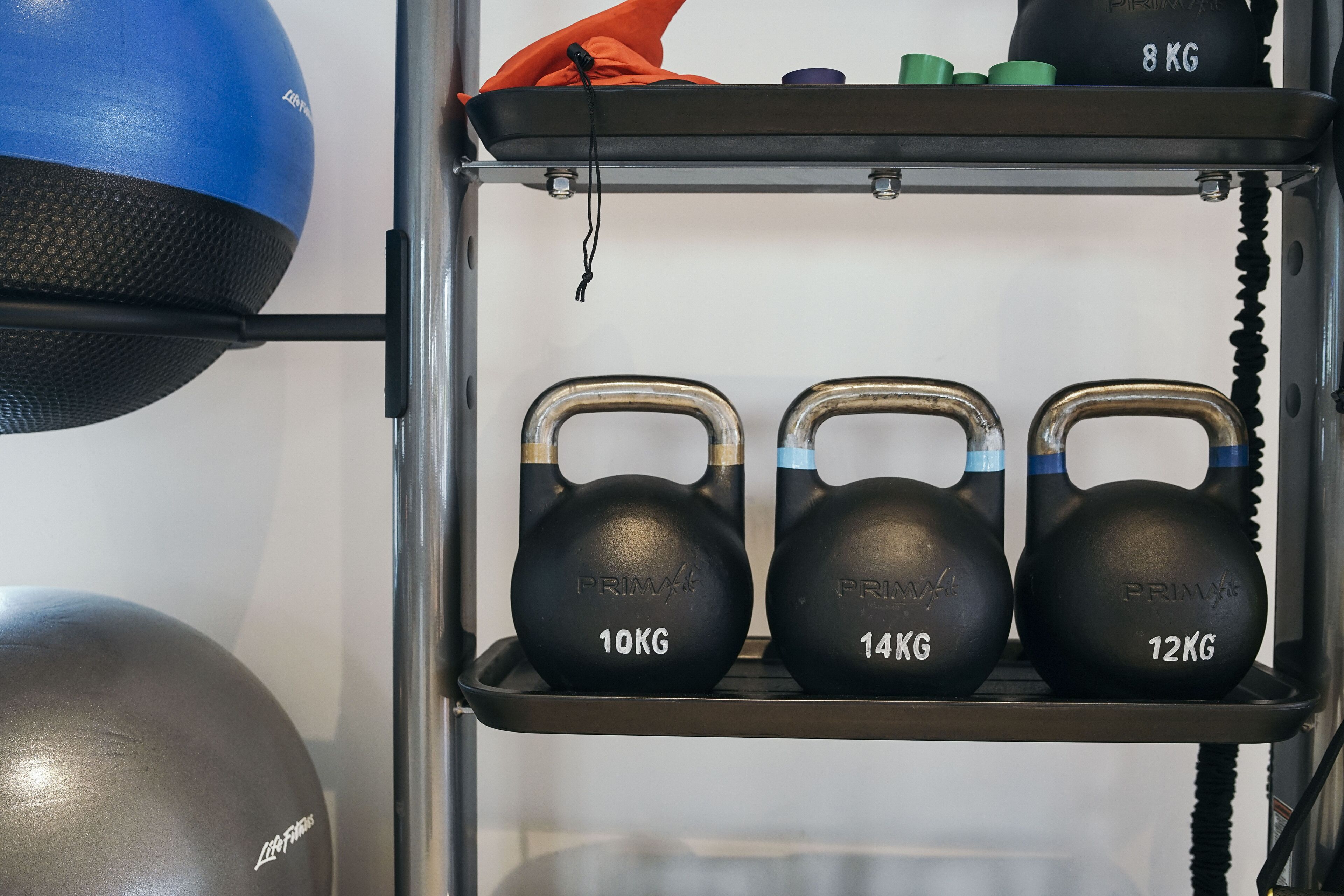 A rack with kettlebells of 10kg, 14kg, and 12kg, and a blue medicine ball.