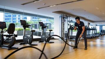 Un gimnasio con equipo de cardio, una máquina de pesas y un amplio ventanal con vistas a edificios.