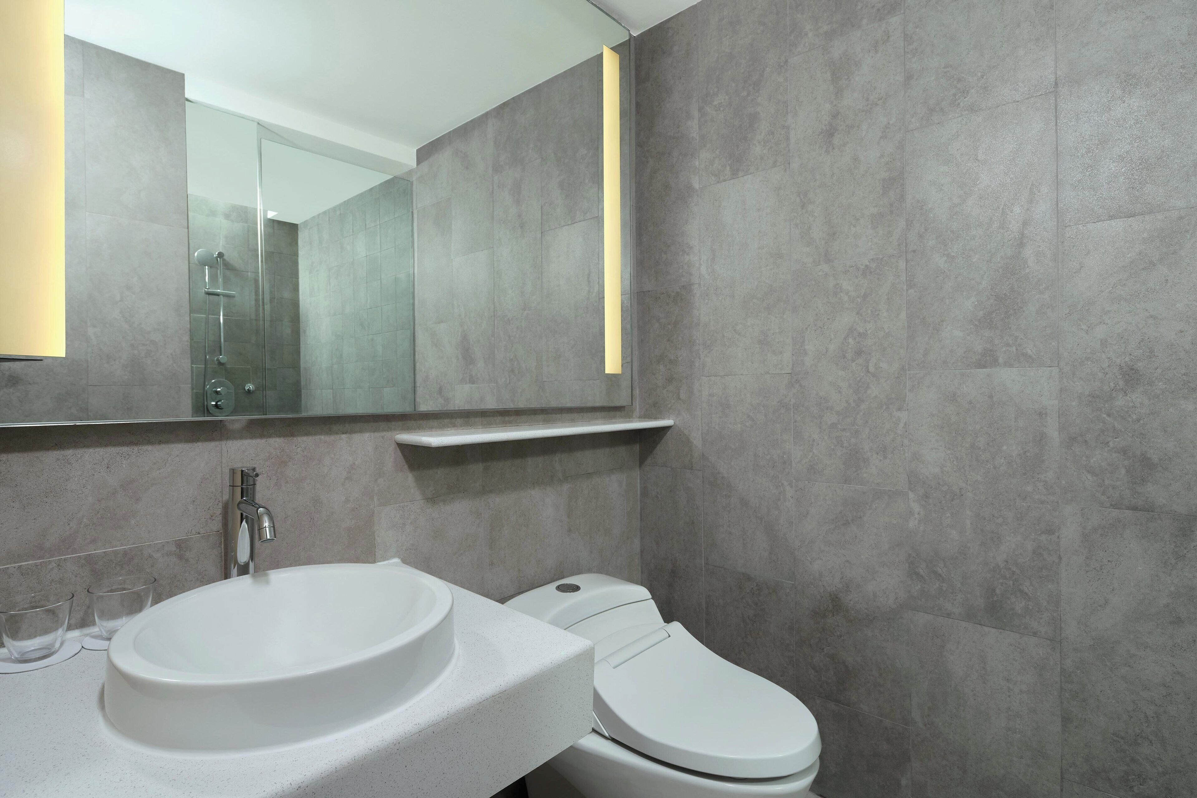 Une salle de bain moderne avec un lavabo blanc, des toilettes et un miroir au-dessus du lavabo.
