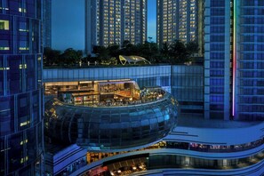 Un hotel moderno con una struttura in vetro dalle linee curve, diversi piani e una terrazza sul tetto con posti a sedere all'aperto.