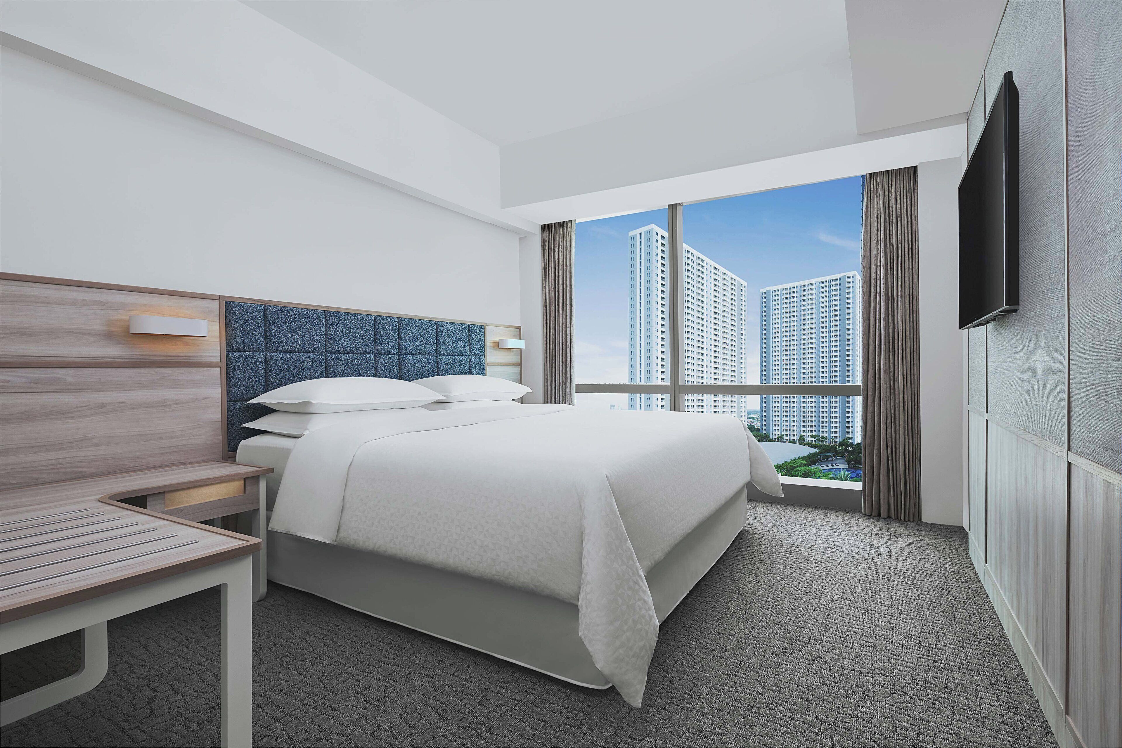 A modern hotel room with a large bed, a desk, and a TV mounted on the wall.