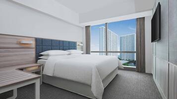 A modern hotel room with a large bed, a desk, and a TV mounted on the wall.