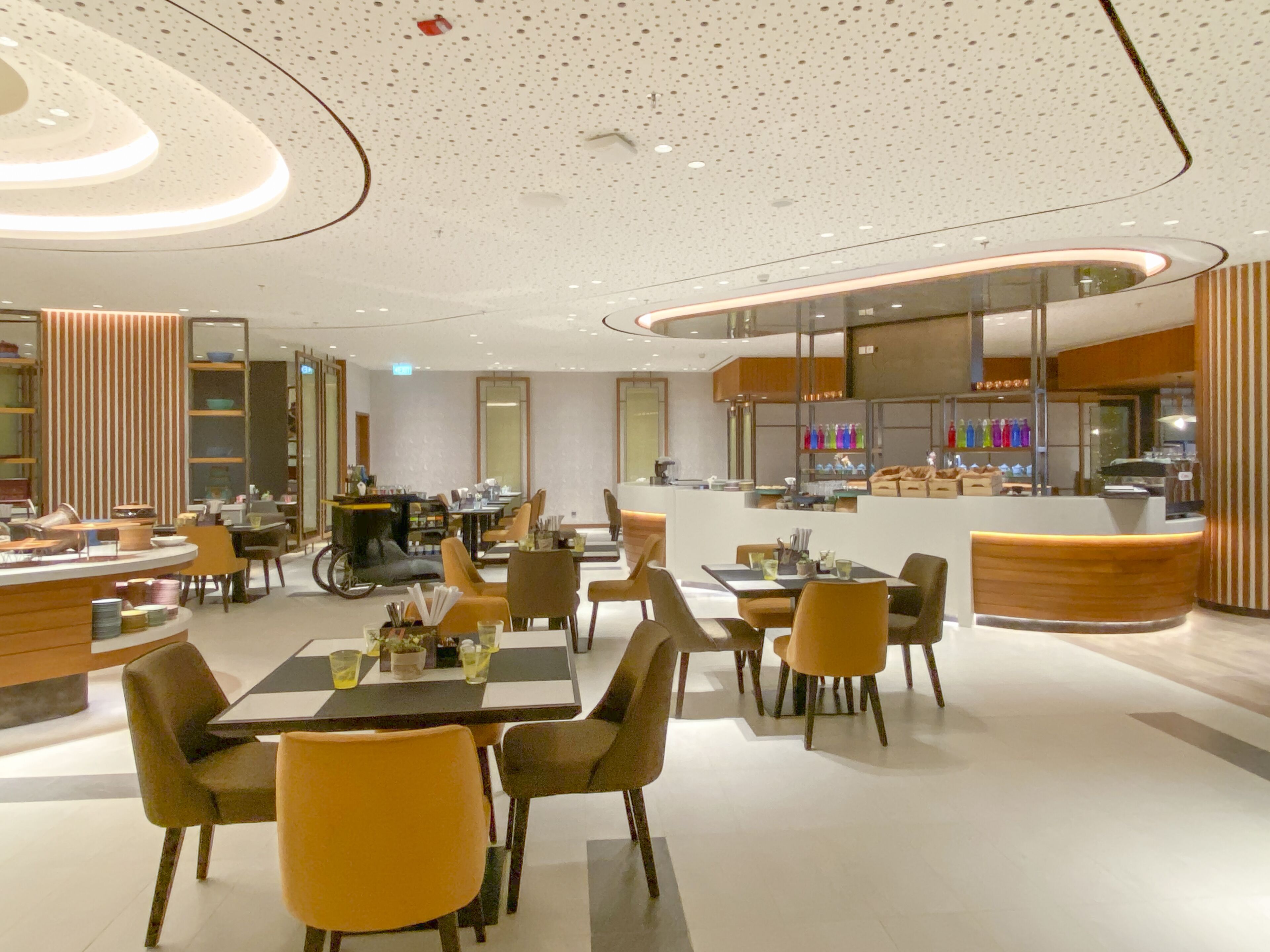 A modern restaurant with a central bar, seating area, and a visible kitchen.