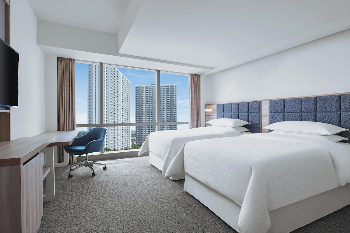 Ein Hotelzimmer mit zwei Betten, einem Schreibtisch, einem Stuhl und einem Fernseher.