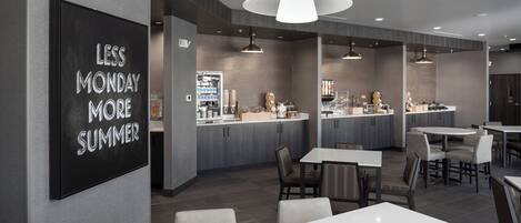 A modern restaurant with a bar area, multiple dining tables, and a prominent sign on the wall.