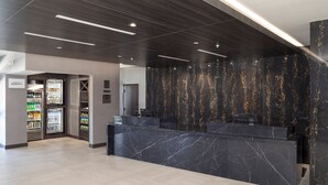 A modern reception area with a marble counter, a refrigerator stocked with beverages, and a wall with a marble pattern.