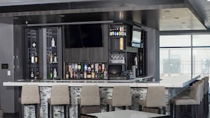 A modern bar area with a long counter, multiple seating options, and a large flat-screen TV mounted on the wall.