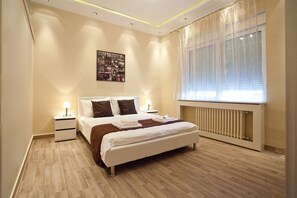 A modern bedroom with a large bed, bedside tables with lamps, a radiator, and a cityscape artwork on the wall. - Feel Belgrade Bohemian Apartment (Belgrade)