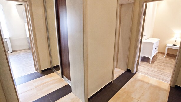 Un couloir au design moderne, avec un sol composé d’un mélange de carreaux clairs et foncés, et un mur blanc avec une porte sur le côté droit.