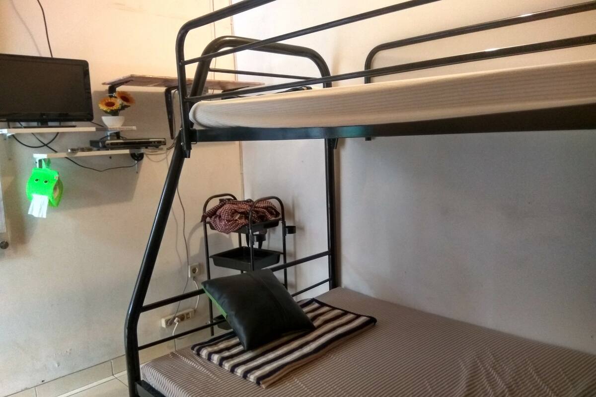 A bunk bed with a mattress, pillows, and a small shelf with a bowl and flowers.