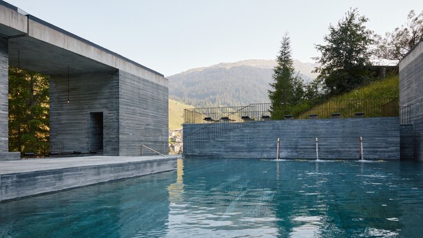 A modern pool area with a concrete structure, a view of mountains, and a metal fence.