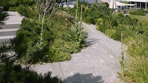 A modern multi-story building with a flat roof and balconies, surrounded by lush greenery and mountains in the background.