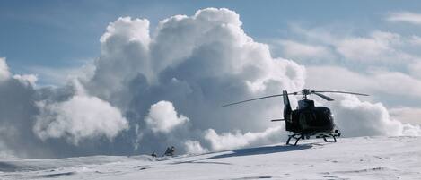 Ein Hubschrauber auf verschneiter Fläche mit einer großen Wolkenformation im Hintergrund.