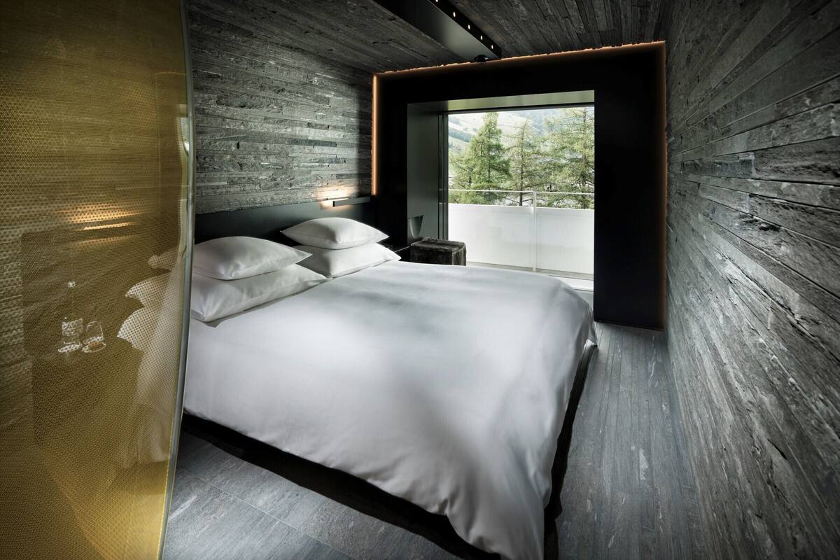 A modern bedroom with a large bed, a view of the outdoors, and a wooden wall.