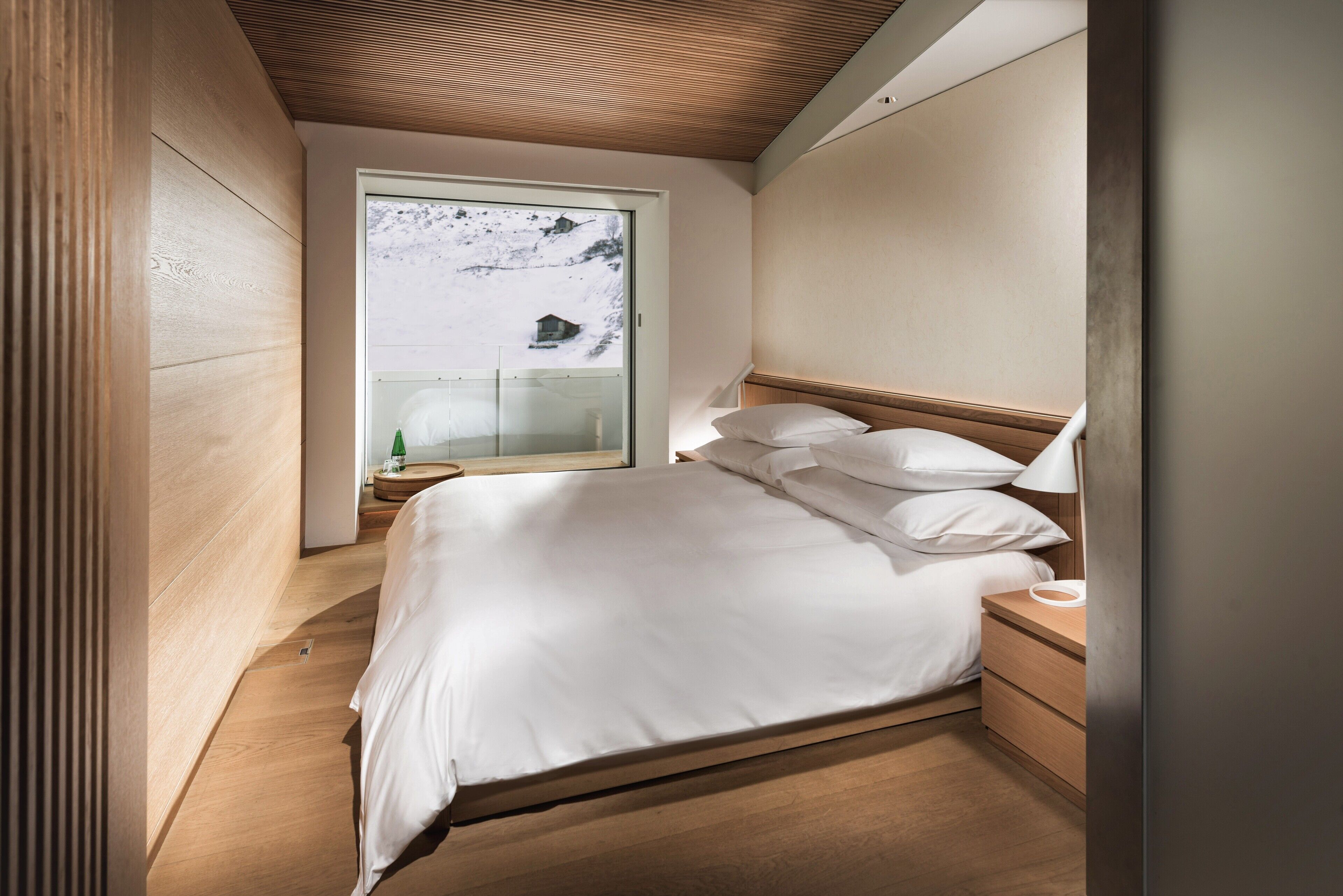 Un dormitorio con una cama de madera, una mesita de noche y una ventana con vistas a un paisaje nevado.