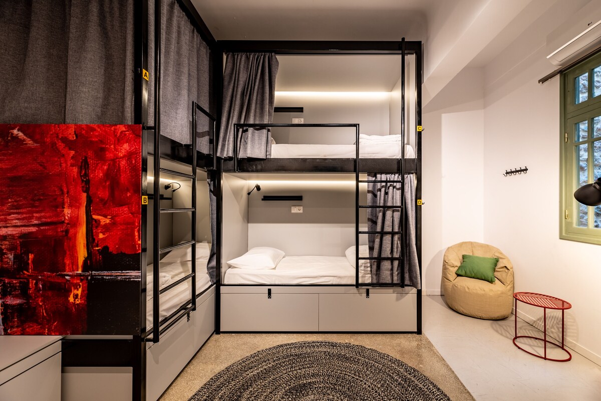 A compact room with a bunk bed, a red metal side table, a green bean bag chair, and a large abstract painting.