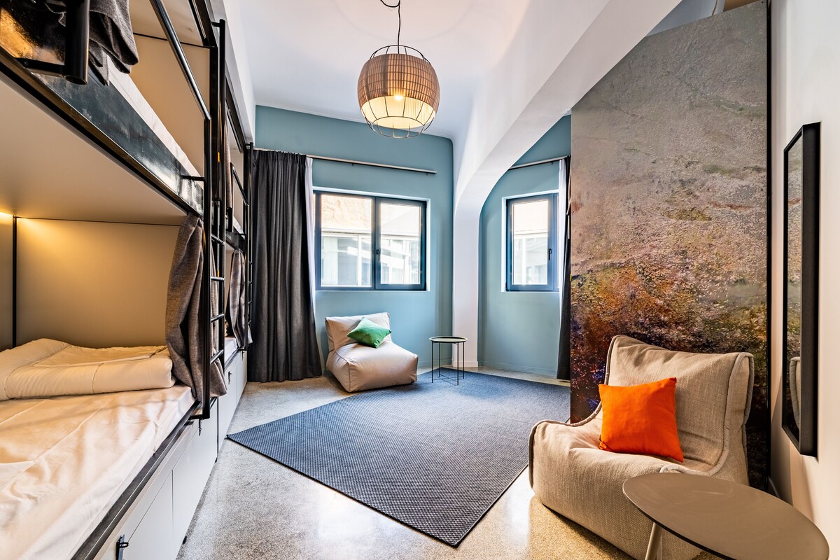A compact room with bunk beds, a sofa, a small table, and a large window.