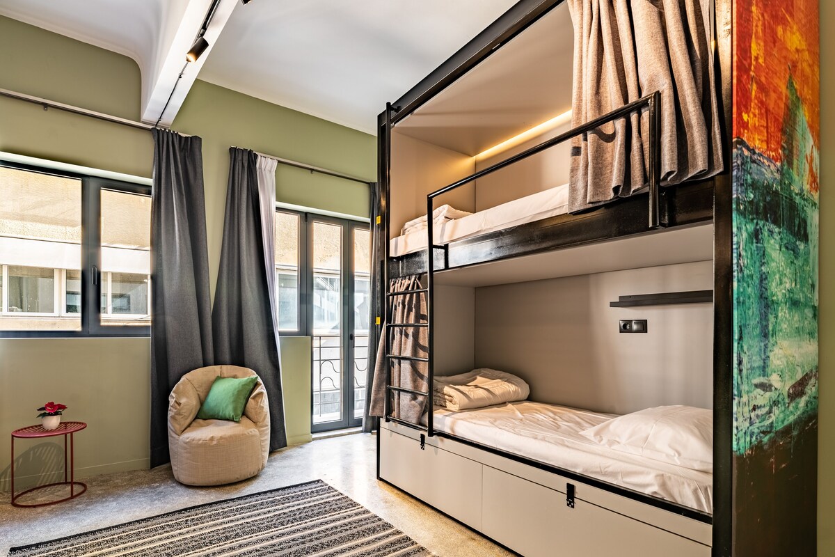 A bunk bed room with a window, a chair, and a small table.