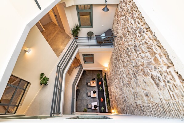 Un intérieur à plusieurs niveaux, avec un mur en pierre, un balcon et un espace salon comprenant des tables et des chaises.