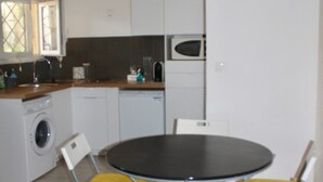 A compact kitchen with a washing machine, a microwave, and a sink. There is a round table with four chairs, two of which have yellow cushions. - T2 fully equipped near all amenities bus, tram, train station, city center (Nice)