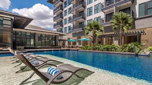 A swimming pool with lounge chairs and umbrellas, surrounded by a multi-story building with balconies. - Dusit Thani Residence Davao (Davao)